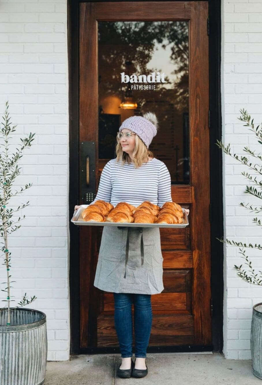 Kristin Hall holding a tray of fresh croissants outside the Bandit Pâtisserie storefront.