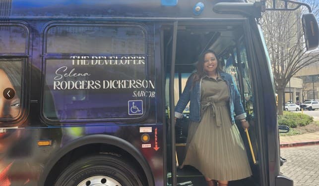 Selena Rogers Dickerson stepping off a transit bus wrapped with her name and the Sarcor branding.