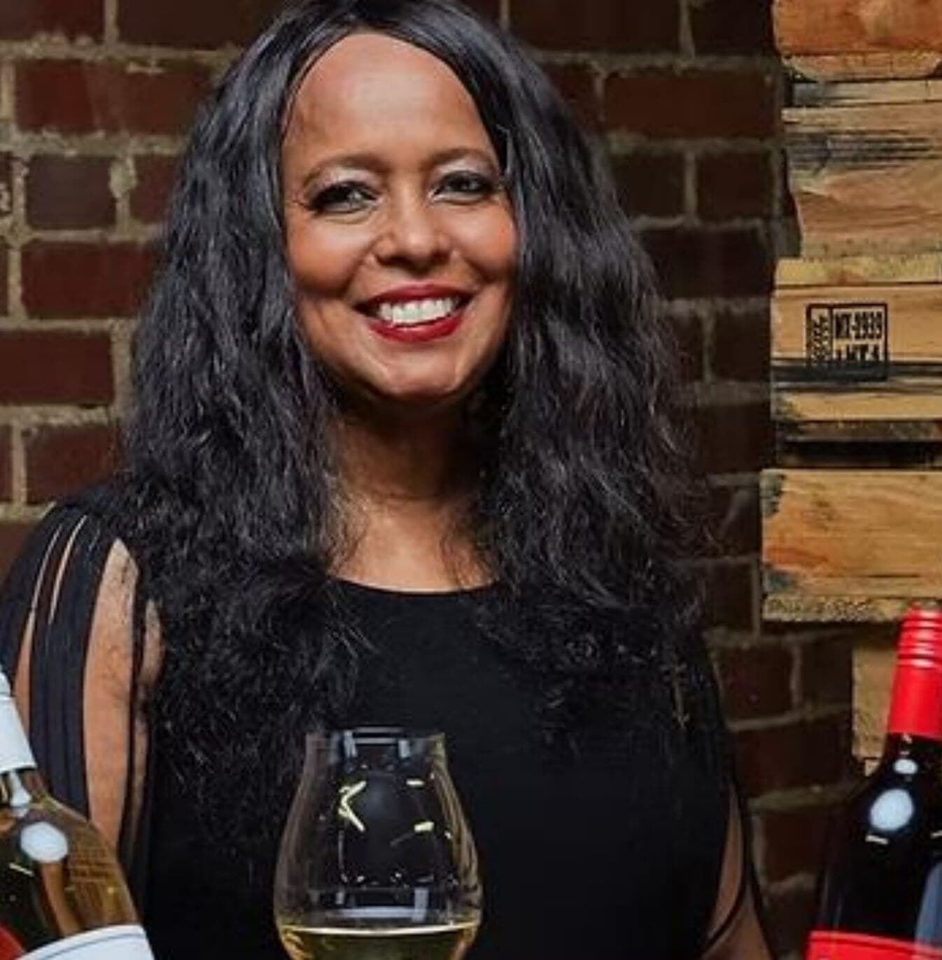 Gwen Hurt, founder of Shoe Crazy Wines & Spirits, smiling beside bottles of her wine.